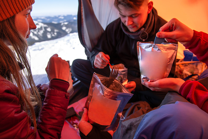 Joyful Friends Having Lunch At Bivouac Camp In Winter Mountains, by Cavan Images / Artur Abramiv