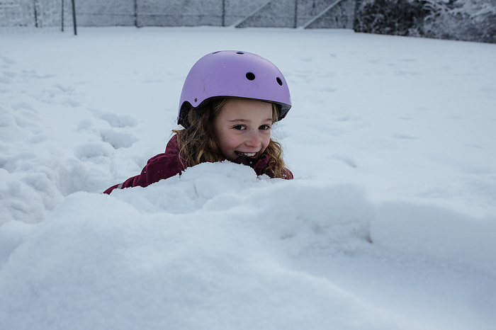girl hiding in the snow whilst ice skating outdoors, by Cavan Images / Rachel Bell