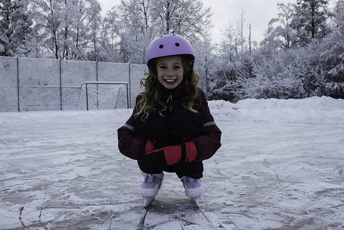 girl on an outdoor ice rink smiling in the snow, by Cavan Images / Rachel Bell