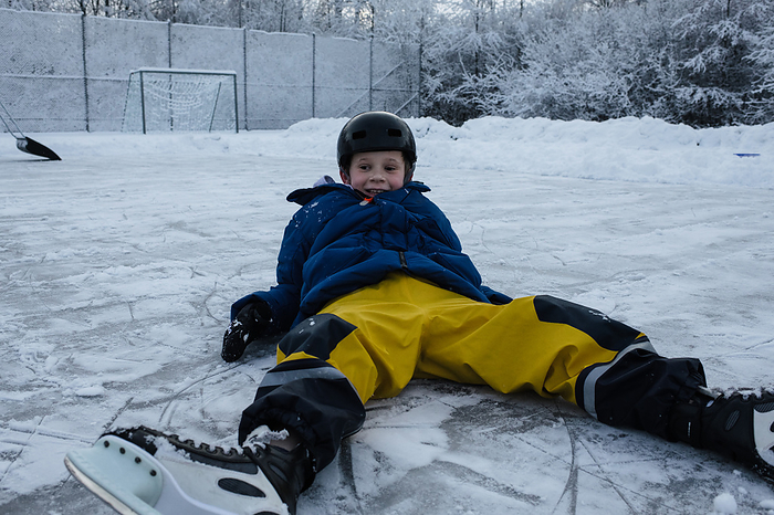 boy laying on the ice ice skating outside, by Cavan Images / Rachel Bell