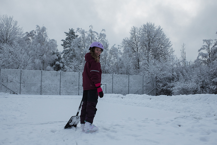 girl with a snow shovel ice skating outside, by Cavan Images / Rachel Bell