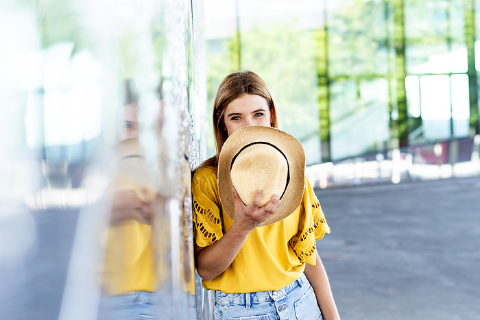 young woman holding a straw hat over her face, revealing just her eyes, by Cavan Images / rafa fernandez