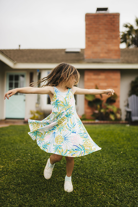 Brown-haired girl spinning in grass in front of house, by Cavan Images / Rachelle Sinn