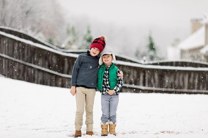 Two brothers playing in the backyard in the snow, by Cavan Images / Jamie Sapp