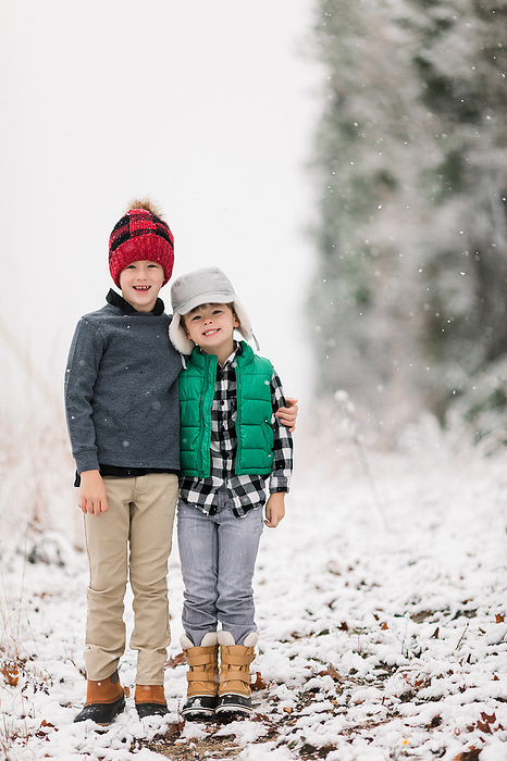 Two brothers smiling in the backyard in the snow, by Cavan Images / Jamie Sapp