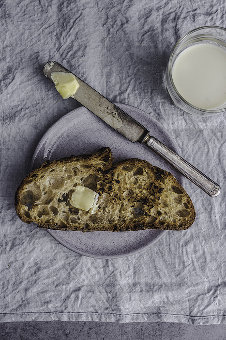 Slice of country bread on a plate with butter, by Cavan Images / Sara Ghedina