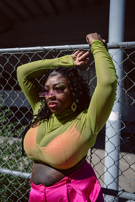 Black woman poses in front of wire fence in harsh sunlight, by Cavan Images / Andrea Guzman
