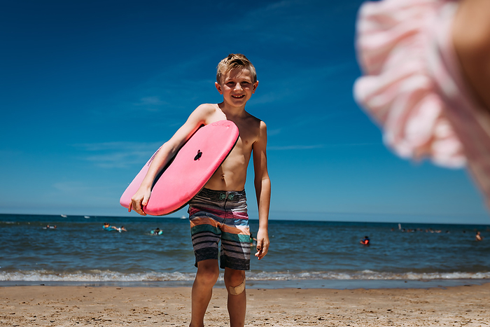 Smiling child on beach of Lake Michigan holding boogie board, by Cavan Images / Krista Taylor
