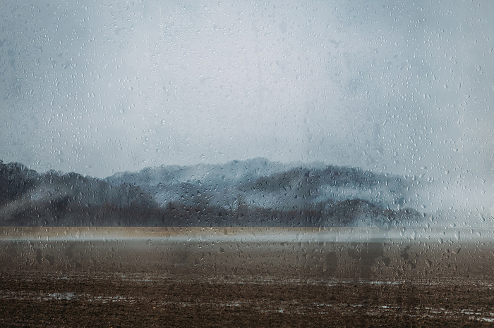 Gloomy landscape through raindrops on window on rainy day, by Cavan Images / Krista Taylor