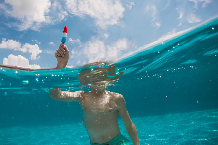 Underwater shot of boy in swimming pool holding popsicle, by Cavan Images / Krista Taylor