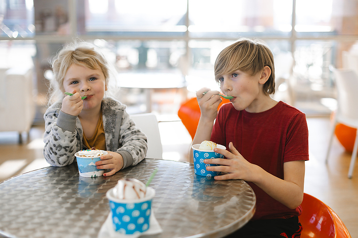 Kids eating icecream in a bright colorful sweet shop, by Cavan Images / Krista Taylor