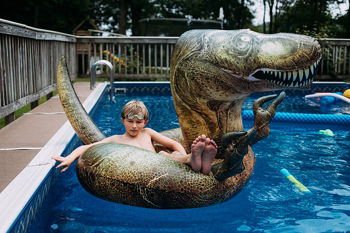 Child on dinosaur pool float in swimming pool, by Cavan Images / Krista Taylor