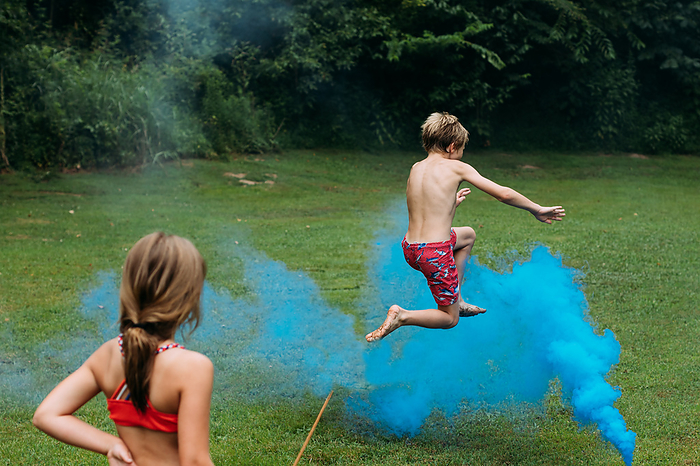 Children playing in smoke bombs on 4th of July in backyard, by Cavan Images / Krista Taylor