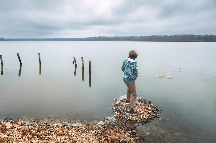 Child skipping rocks on shore of lake during winter day, by Cavan Images / Krista Taylor