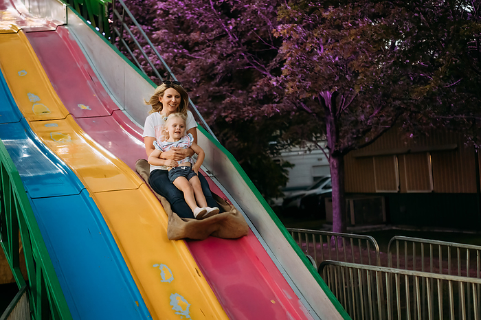 Mom and daughter sliding down fun slide at carnival, by Cavan Images / Krista Taylor