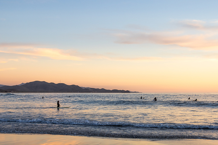 Surfers enjoy calm waves at sunset., by Cavan Images / Michael Hanson