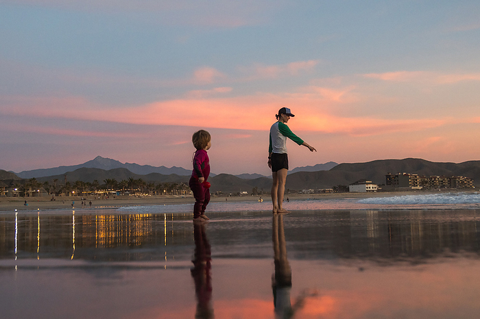 A mother and son walk on the beach at sunset., by Cavan Images / Michael Hanson