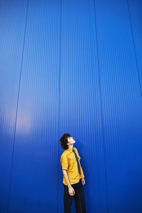 young man in a yellow shirt looking up against a blue wall, by Cavan Images / Elena Perevalova