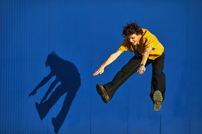 smiling young man in a yellow shirt jumping on a blue background, by Cavan Images / Elena Perevalova