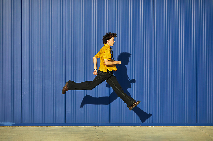 smiling young man in a yellow shirt jumping on a blue background, by Cavan Images / Elena Perevalova