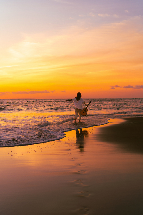 Woman musician with guitar on the beach at sunset. Bali, by Cavan Images / Yuliya Kirayonak