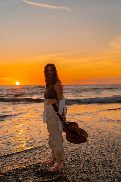 Woman musician with guitar on the beach at sunset. Bali, by Cavan Images / Yuliya Kirayonak