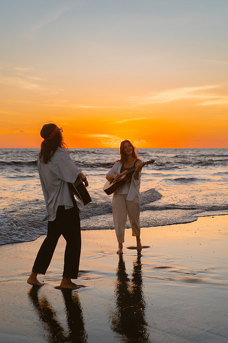 Women friends play guitars on the beach. Sunset on the ocean. Bali, by Cavan Images / Yuliya Kirayonak