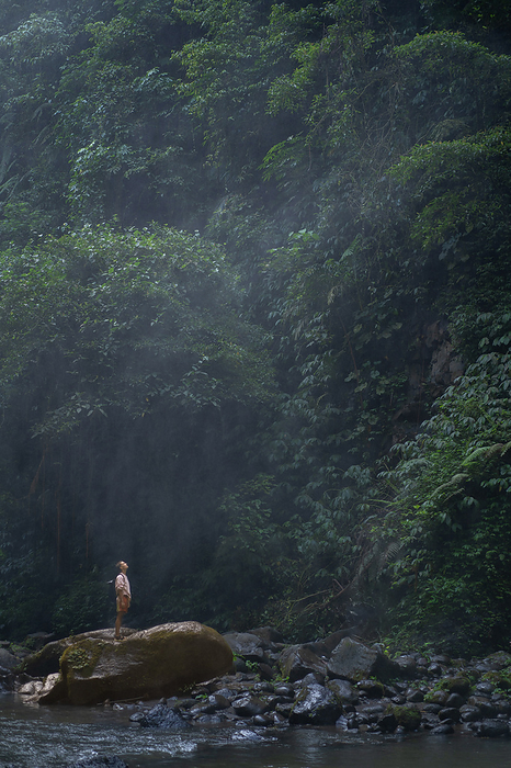 Woman traveler, explorer stands on rock in jungle, looks at waterfall., by Cavan Images / Yuliya Kirayonak