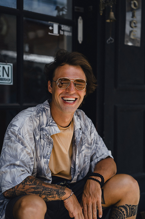 Young, handsome, romantic, laughing man in yellow sunglasses., by Cavan Images / Yuliya Kirayonak