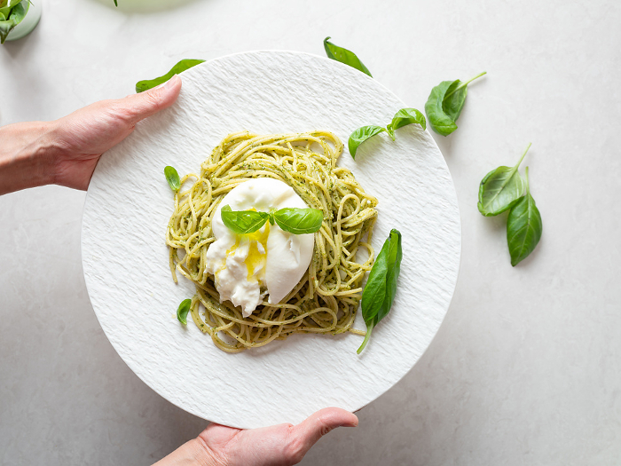 Woman's hand holding Genovese pasta topped with blatter cheese
