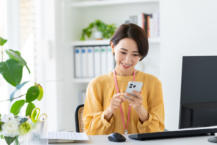 Middle Japanese businesswoman using smartphone in office （Female / People)