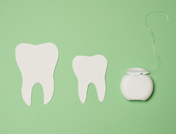Dental floss and paper teeth on green background, oral hygiene, top view Dental floss and paper teeth on green background, oral hygiene, top view