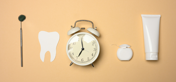Alarm clock, tube of toothpaste and paper tooth on brown background, oral hygiene care, top view Alarm clock, tube of toothpaste and paper tooth on brown background, oral hygiene care, top view