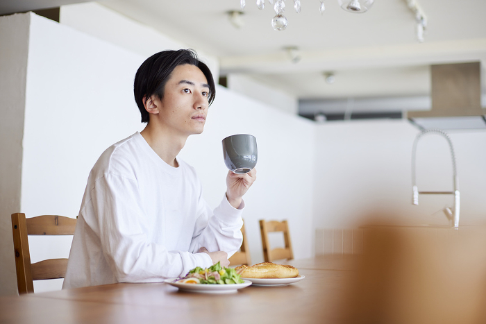 Young Japanese man eating breakfast in the living room (People)