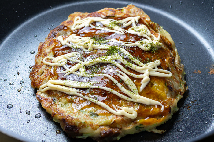 Okonomiyaki cooked in a frying pan. Sauce, mayonnaise and aonori seaweed.