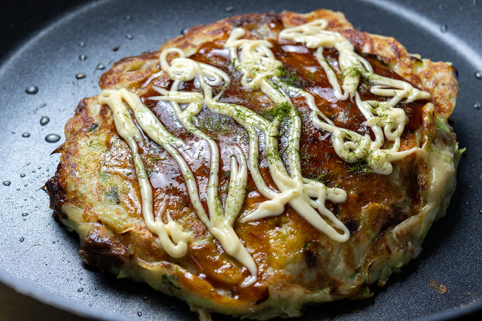 Okonomiyaki cooked in a frying pan. Sauce, mayonnaise and aonori seaweed.