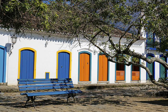View to colonial house facades with colorful wooden doors in sunshine with a blue bench and tree bra View to colonial house facades with colorful wooden doors in sunshine with a blue bench and tree bra, by Zoonar Uwe Bergwitz
