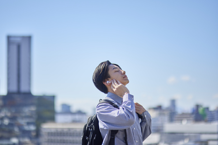 A male Japanese university student on his way to school listening to music through wireless earphones (People)
