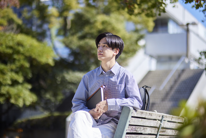 A male Japanese university student sitting on a bench on a university campus (People)