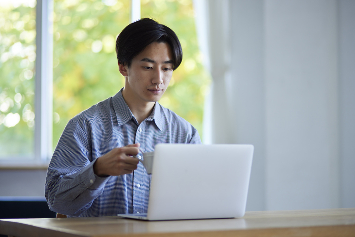 A male Japanese university student using a computer in the living room.
