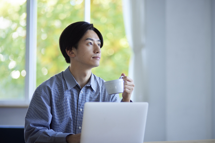 A male Japanese university student using a computer in the living room.