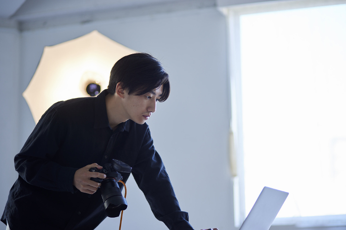 Japanese male photographer operating laptop computer in photo studio (People)