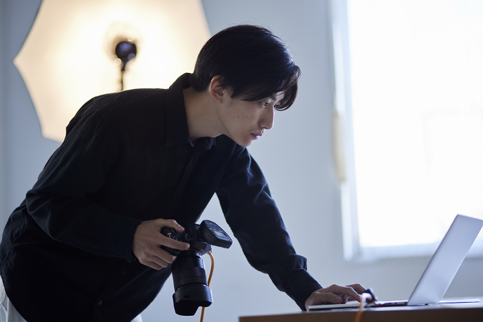 Japanese male photographer operating laptop computer in photo studio (People)