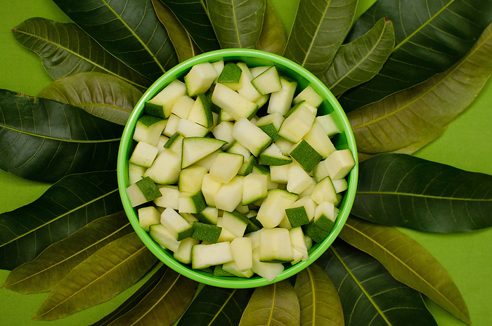 Raw mango pieces in Green bowl with mango tree leaves on Green background Raw mango pieces in Green bowl with mango tree leaves on Green background, by Zoonar RealityImages