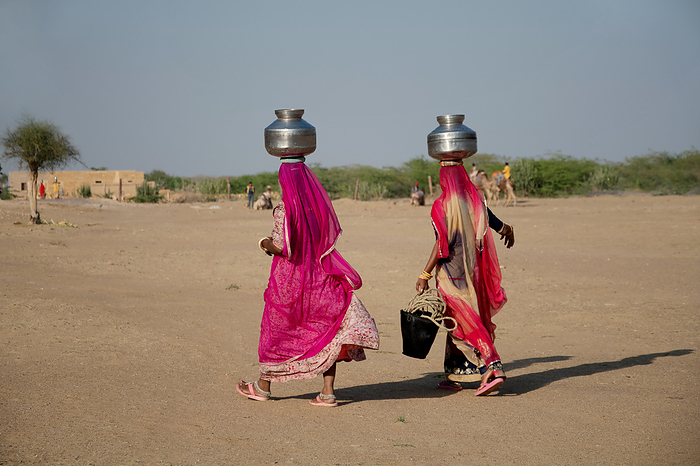 Two woman carrying water in steel vessels on head  in desert, Khuri, Rajasthan, India Two woman carrying water in steel vessels on head  in desert, Khuri, Rajasthan, India, by Zoonar RealityImages