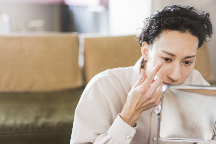 Young Japanese man putting on contact lenses at home (People)