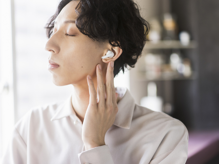 Japanese man in his 20s listening to music with wireless earphones.