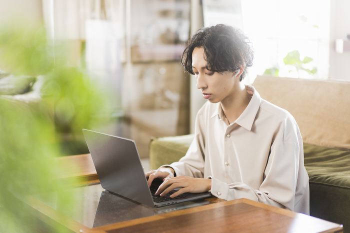 Young Japanese man working on his laptop at home (People)