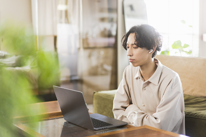Young Japanese man working remotely from home using a laptop computer (People)