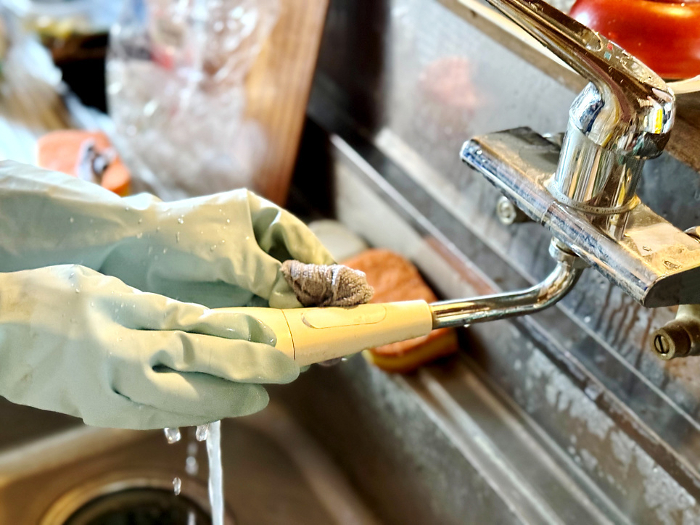 Hands with plastic gloves cleaning a dirty faucet